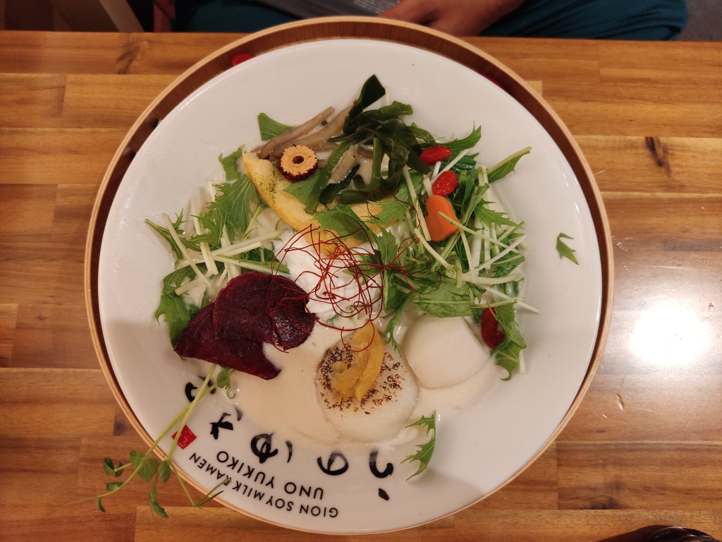 A creamy broth topped with beetroot crisps, a triangle of tofu, lots of greens, and a rice cake