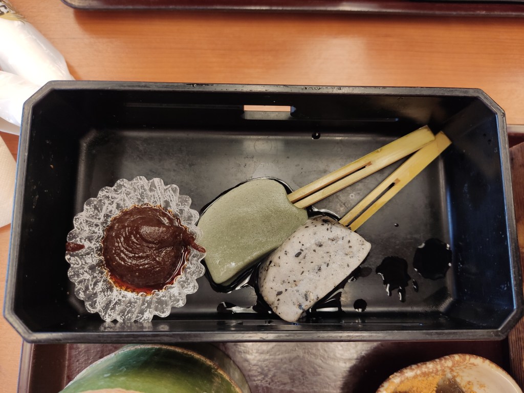 A small cake case filled with a dark brown paste alongside two things that look like lollipops, one with a green sweet and the other white flecked with black