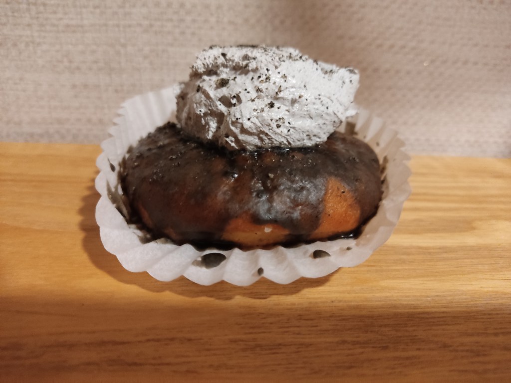 A donut with a dark brown glaze and a gray dollop of cream
