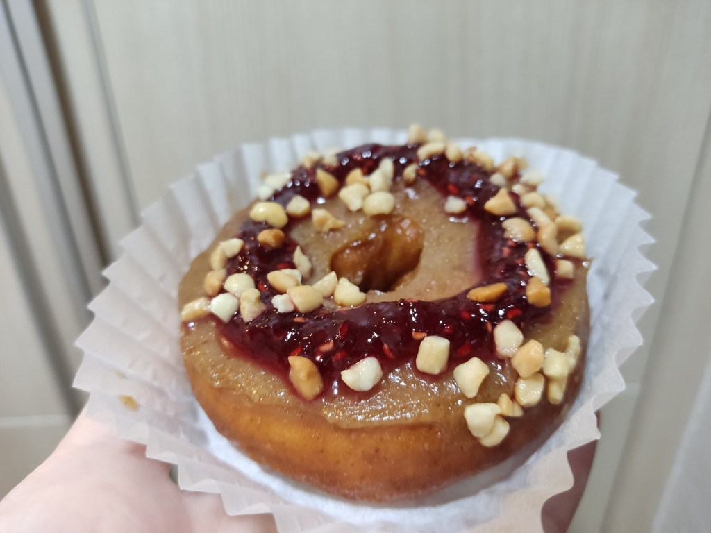 A donut with peanut butter icing, a ring of red jam, and chopped nuts