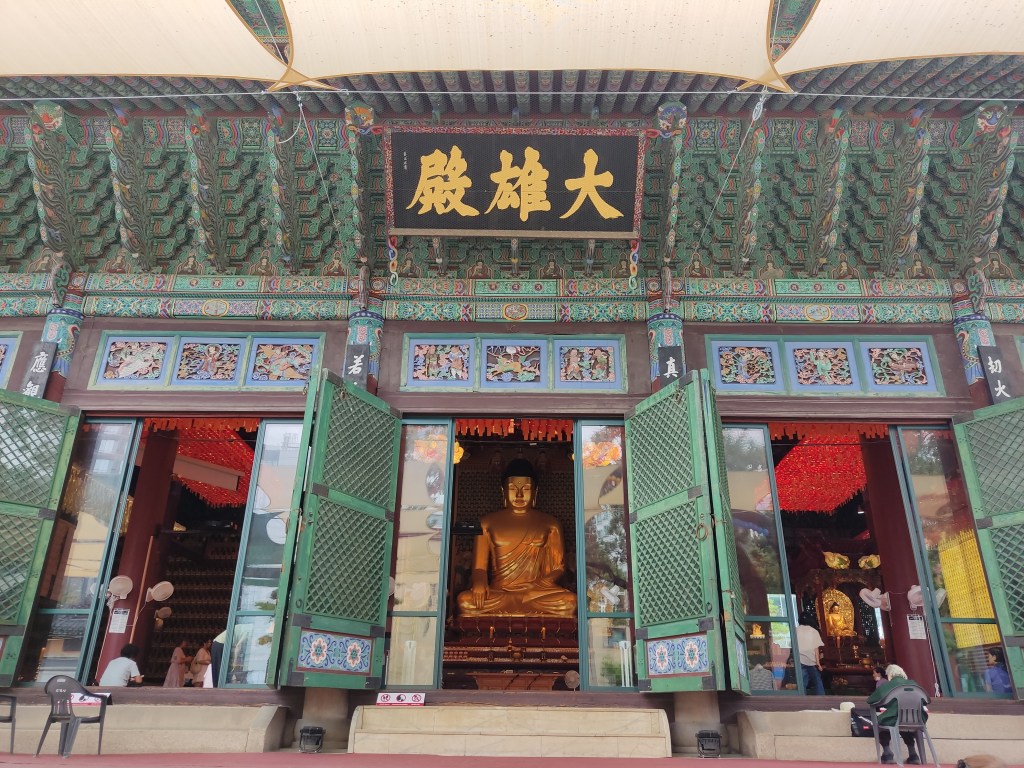 An ornate building in the temple with a statue of Buddha visible through the door