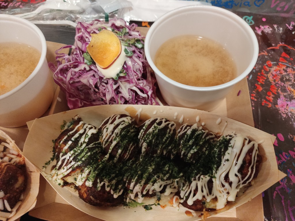 8 takoyaki balls drizzled with a lot of sauce and seasoning, served with a small cup of soup and a big heap of red cabbage salad