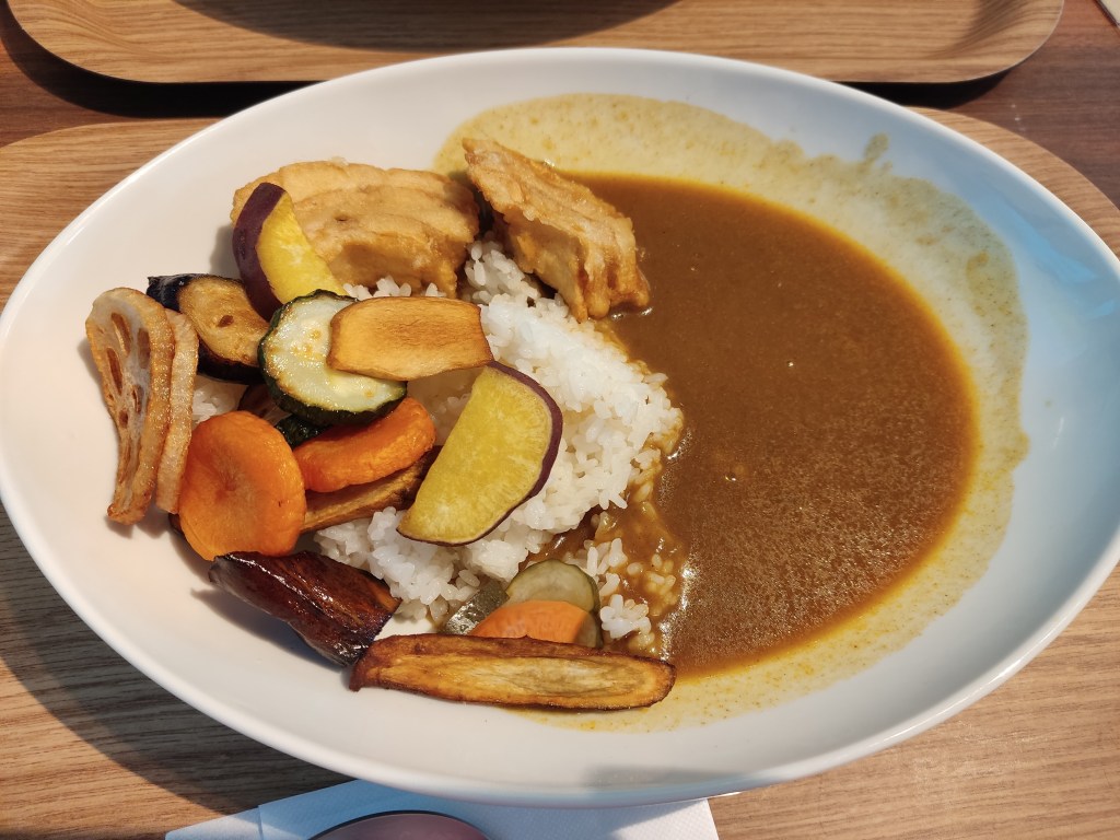 A pile of rice topped with roasted and fried vegetables and mock meat, with a rich yellowish brown curry sauce