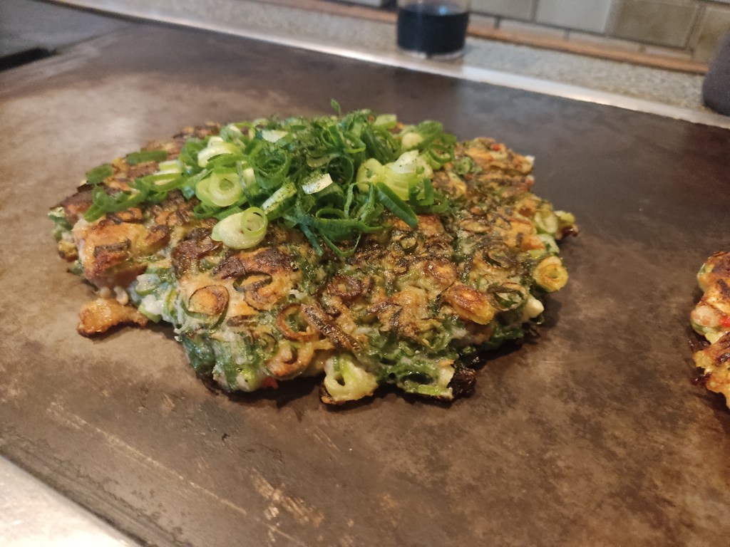 A thick green onion pancake cooking on a grill