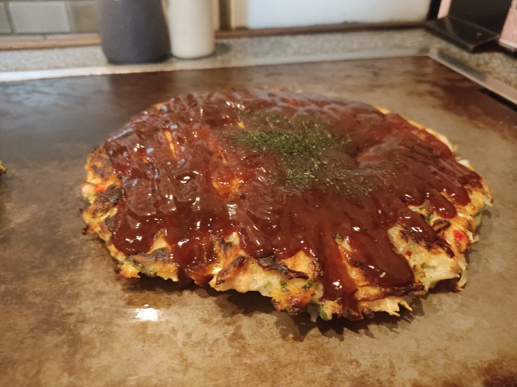 A thick pancake covered in sauce cooking on a grill