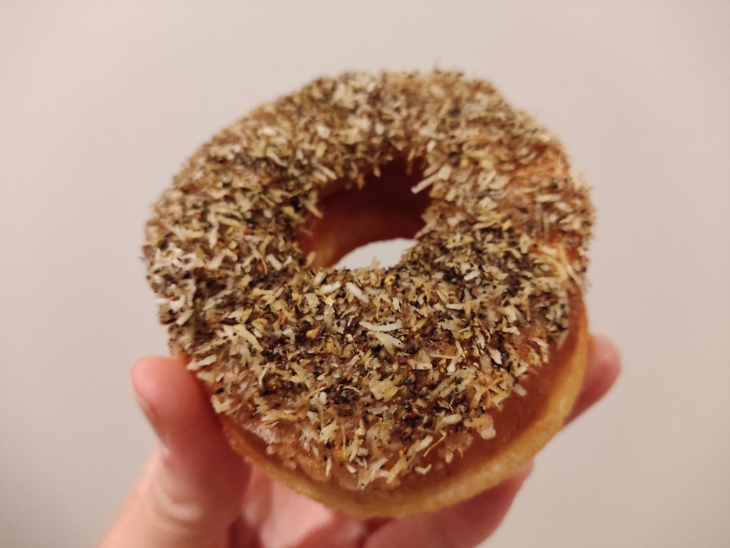 A ring donut topped with dessicated coconut and a spice blend