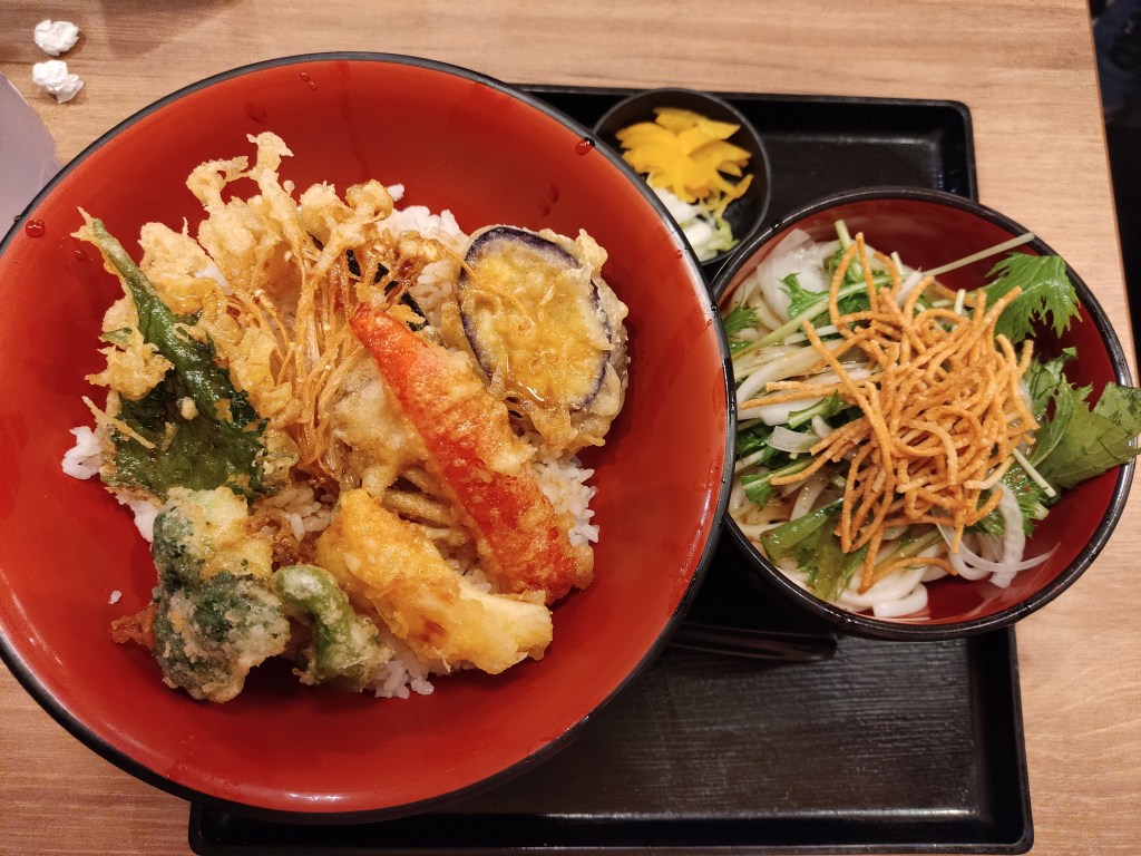 A big bowl of tempura vegetables, a small bowl of pickles, and a medium bowl with salad topped with crispy noodles