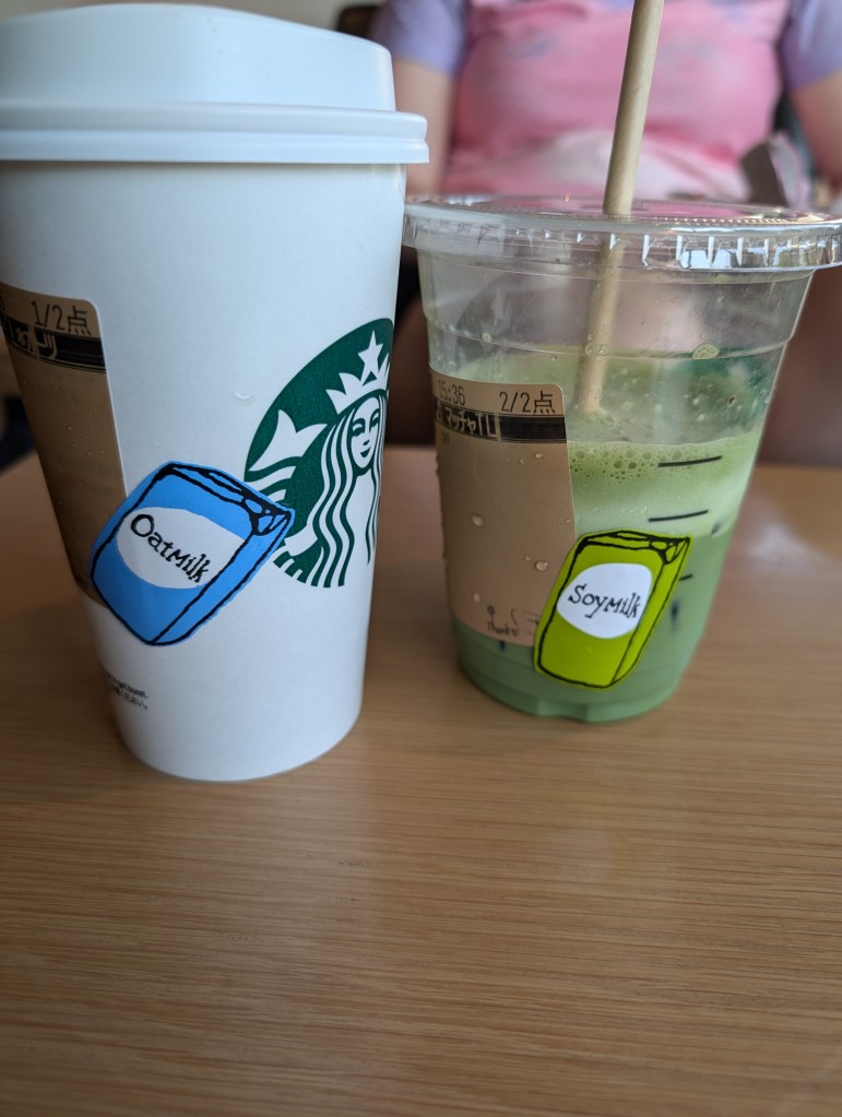 Two Starbucks takeaway cups one with an oat milk sticker and the other with a soy milk sticker