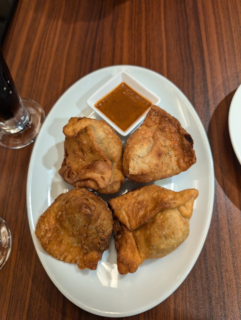 Four browned samosas and a brown dipping sauce