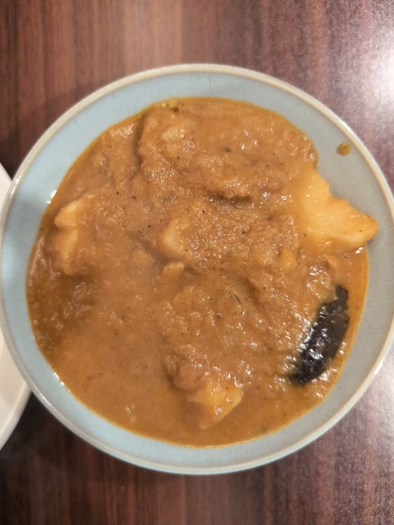 A bowl of aubergineand potato curry, with big chunks of potato and aubergine poking out of an orange gravy