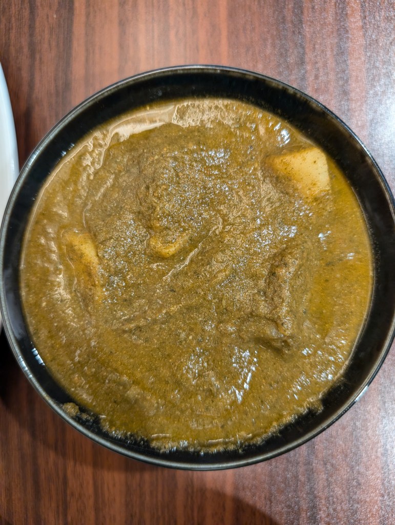 A bowl of spinach and potato curry, with big chunks of potato poking out of a green gravy