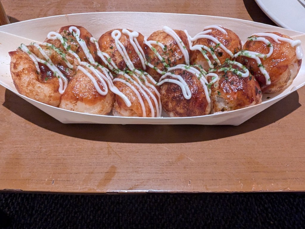 Ten takoyaki balls drizzled with sauce and herbs