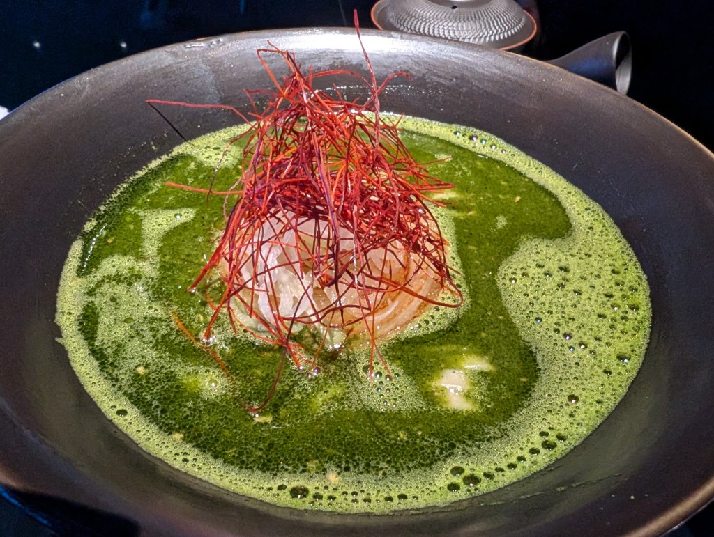 A vivid green broth topped with noodles and chilli threads