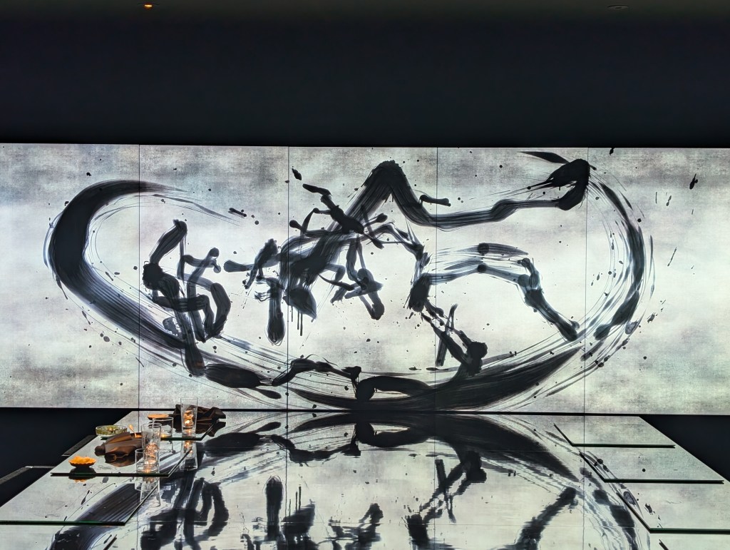 Digital artwork showing calligraphy in motion in a dark room, with the art work reflecting on the dining table.