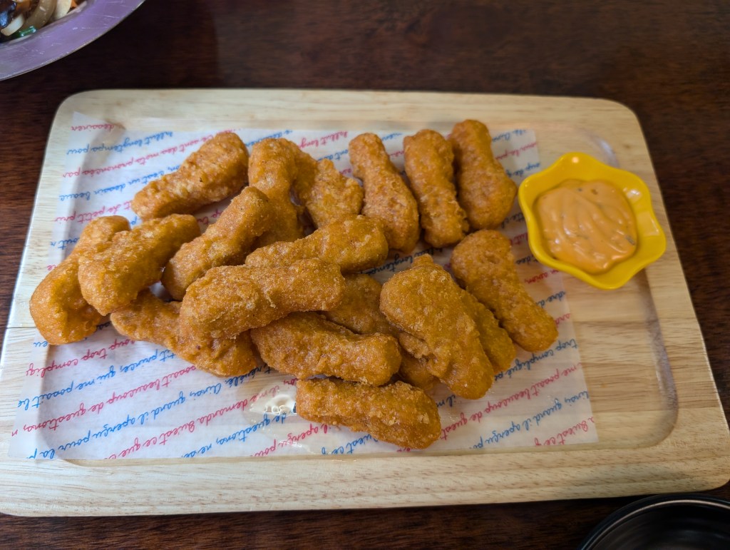 Battered chicken shaped like small drumsticks with a creamy orange sauce on the side