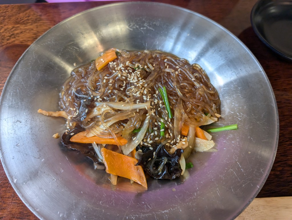 A bowl of japchae with glass noodles and vegetables