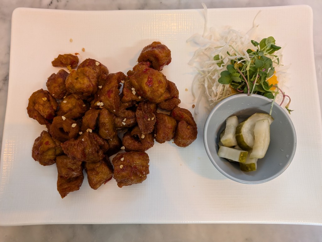 A plate with fried chicken sprinkled with chilli and served with pickled cucumber and salad