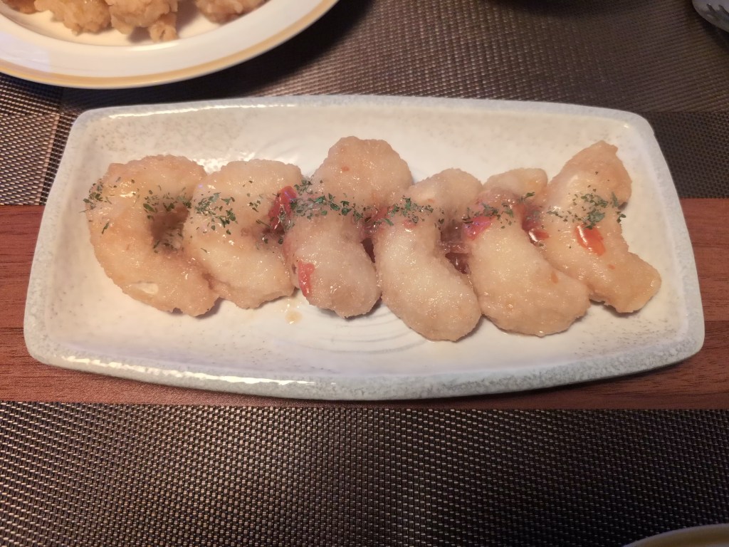 Six battered shrimp with a drizzle of red sauce and green herbs