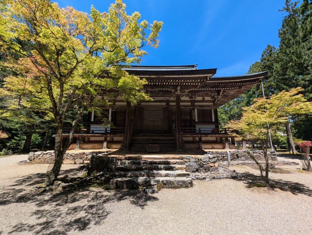 A traditional building at a temple surrounded by trees with a bright blue sky ahead