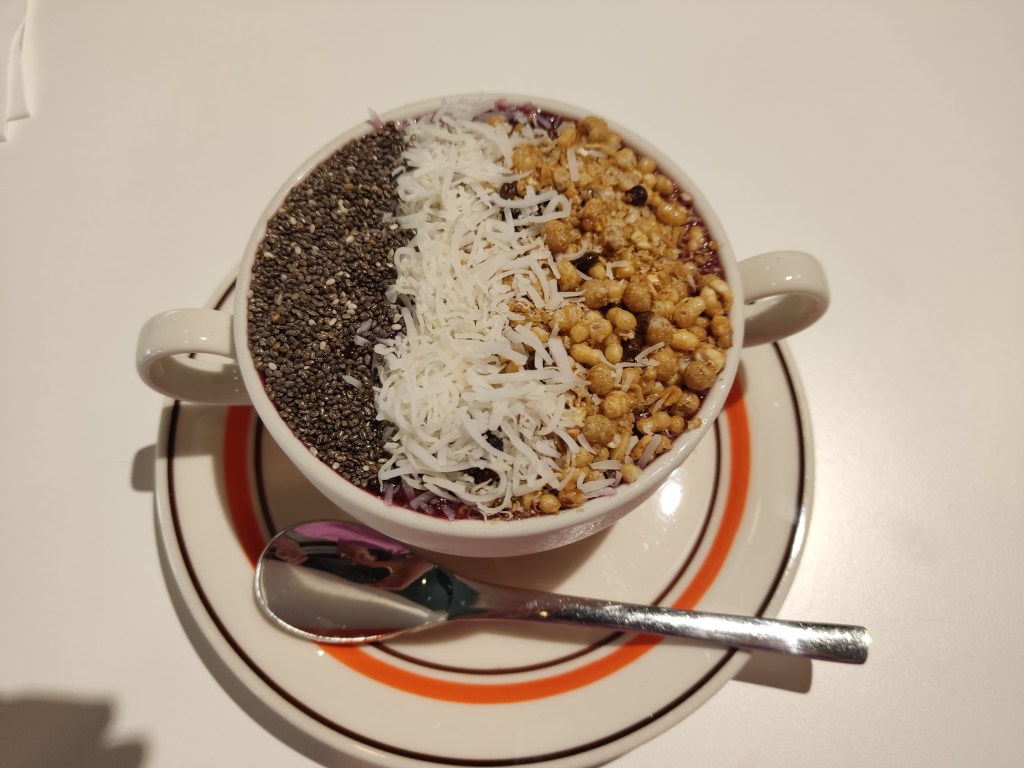 A bowl of purple smoothie, topped with seeds, shredded coconut, and sticky puffed rice