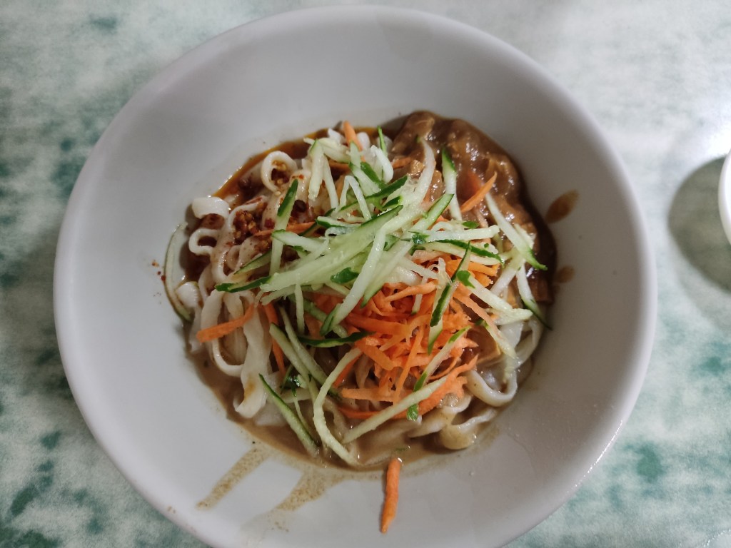 Thick white noodles in sauce and topped with thin shards of cucumber and carrot