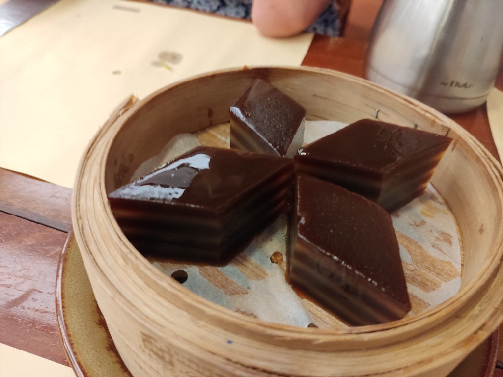 A steamer containing four pieces of gelatinous looking striped brown cake