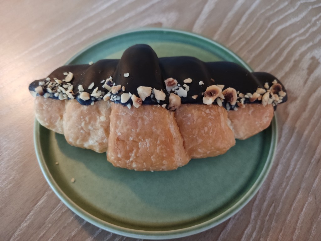 A croissant half dipped in chocolate and topped with a line of chopped nuts