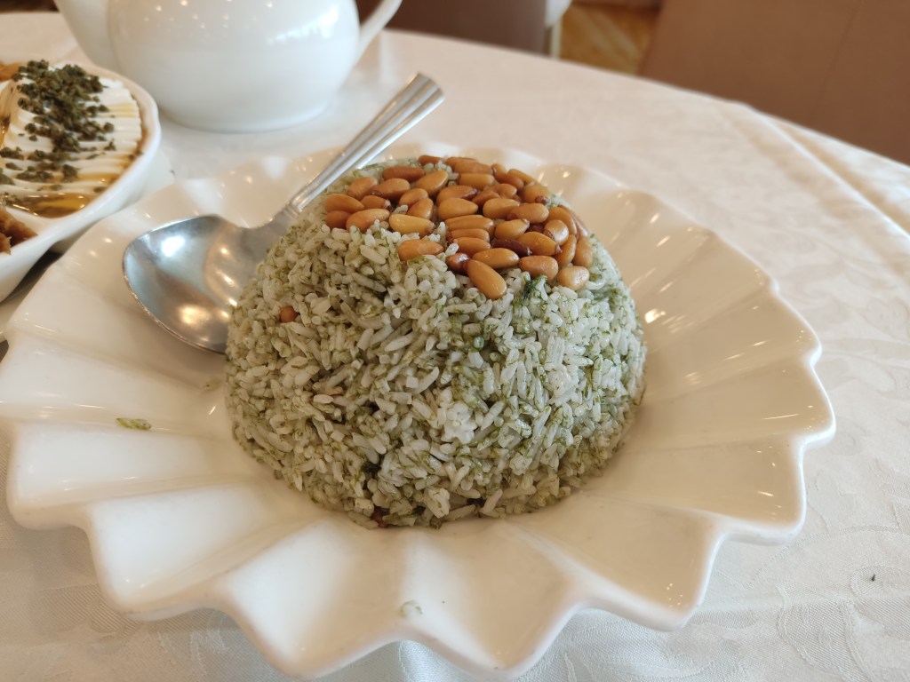 A dome of rice speckled with green and topped with pine nuts