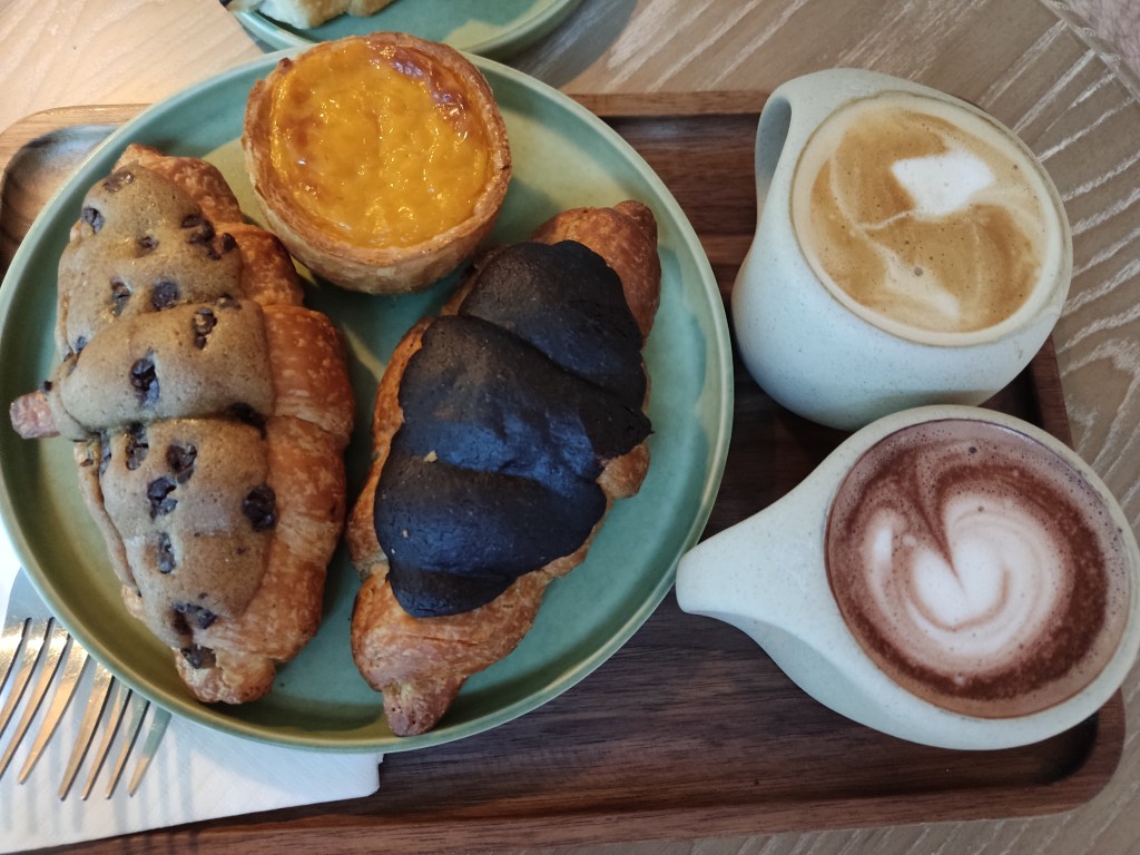 A plate containing three pastries alongside two milky, frothy hot drinks
