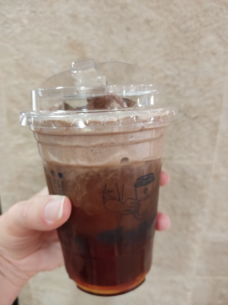 A plastic takeaway cup filled with brown tea and topped with a thick layer of cream