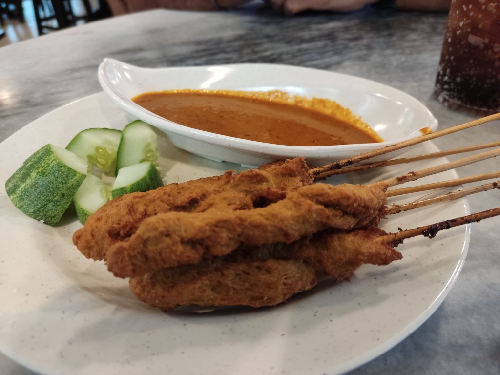 Satay skewers alongside a dip and cucumber