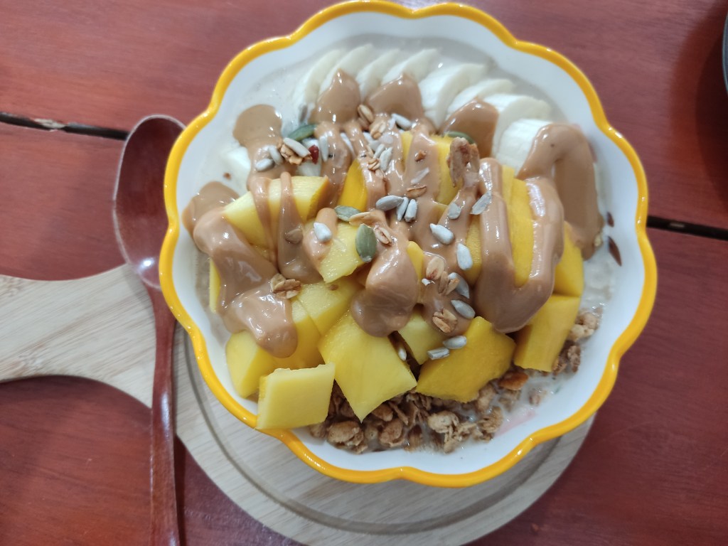 A bowl topped with granola, fruit, and peanut butter
