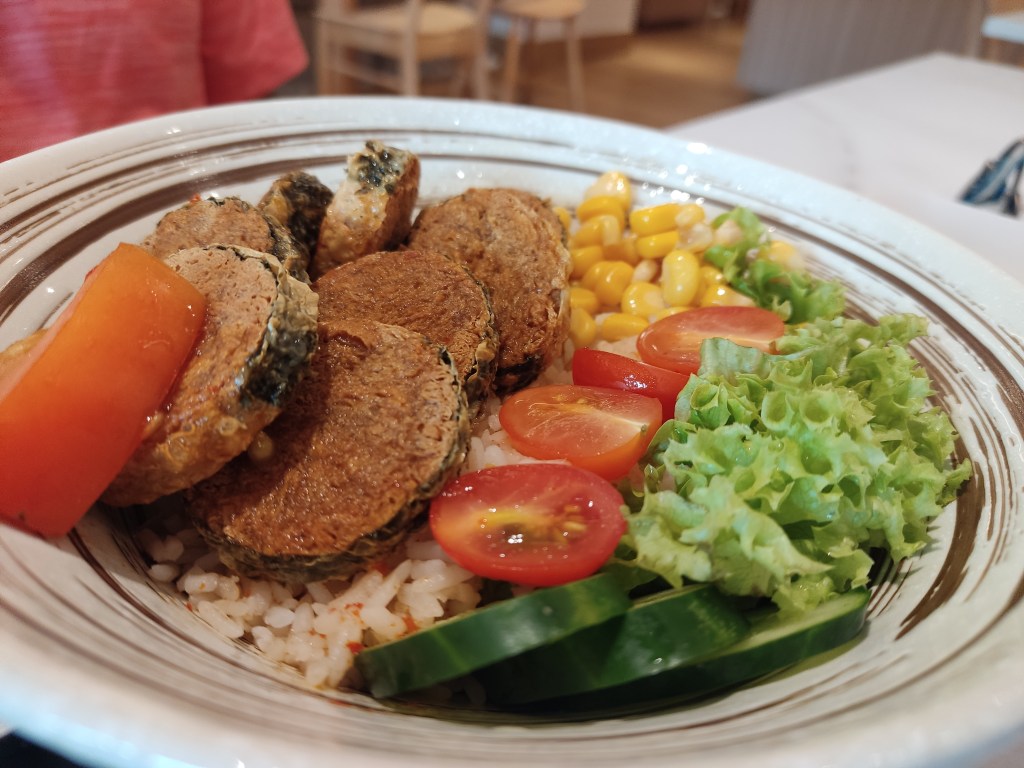 A bowl of rice topped with vegetables and fried fishy slices