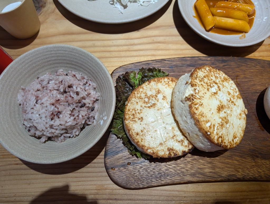 Two large browned slabs of tofu with a bowl of purplish rice