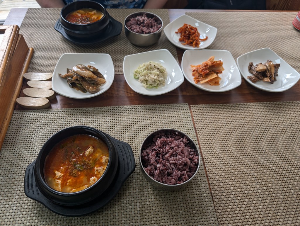 Two portions of tofu stew with five plates of banchan in the middle of the table