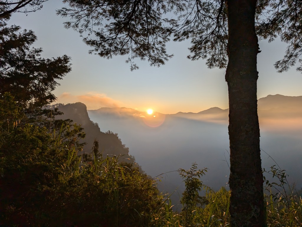 Sunrise with the sun peeking over a mountain and a blanket of clouds below