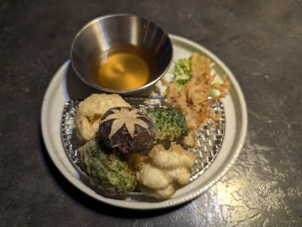 A plate of tempura and pot of dipping sauce