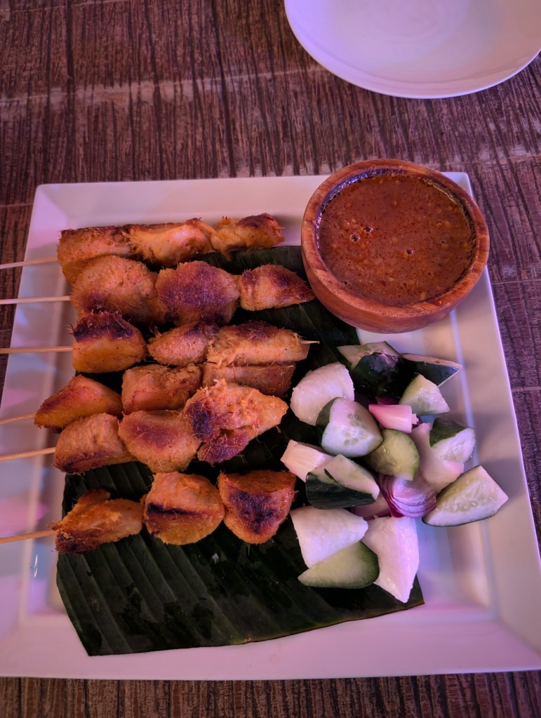 Six chicken skewers, a pot of satay sauce, and some salad
