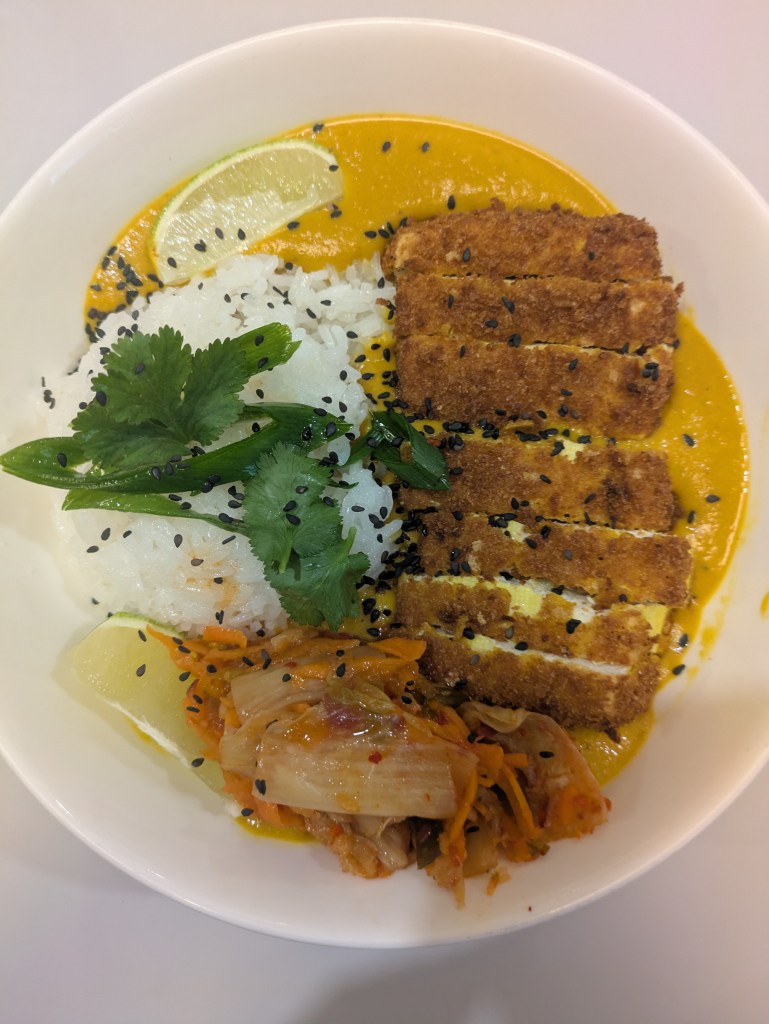 A bowl of katsu curry with white rice, yellow sauce, and crispy coated tofu