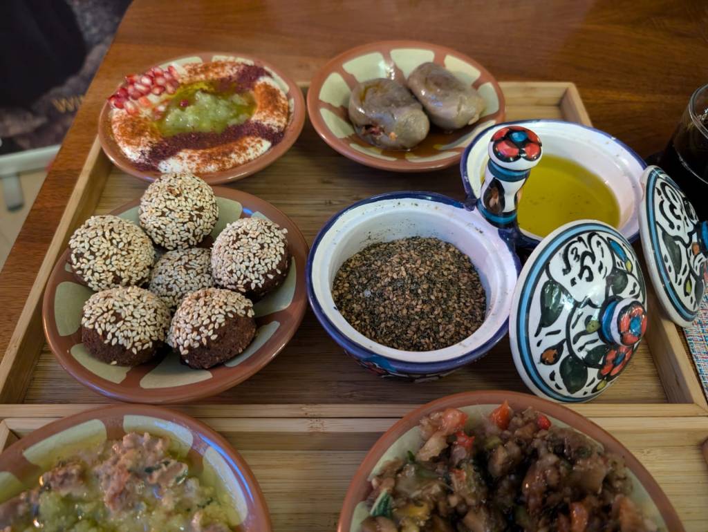 A tray with four dishes: hummus, makdous, zatar and oil, and falafel