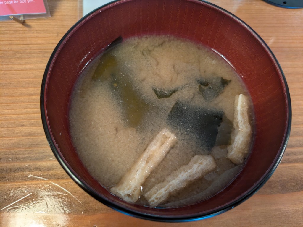 A bowl of cloudy miso soup with bits of seaweed and tofu 