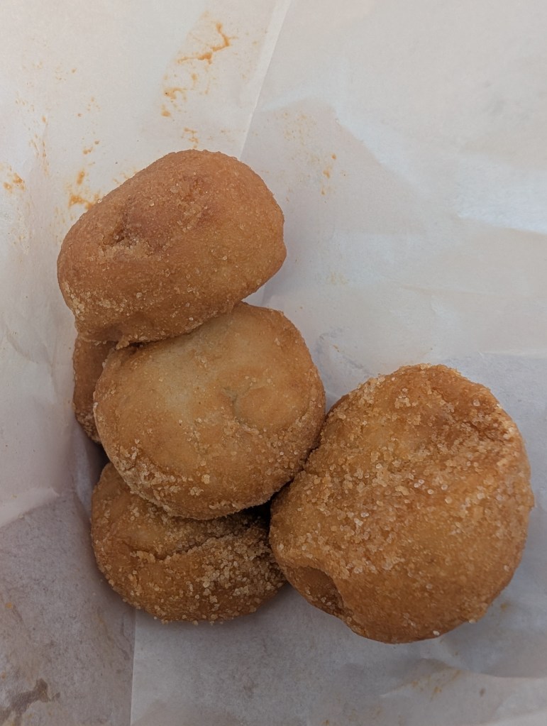 A paper bag of five donut holes with flour on them