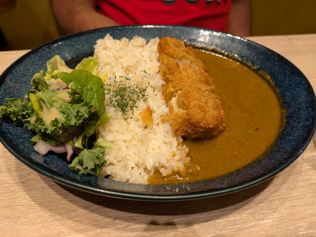 A bowl of side salad, rice, and curry sauce with katsu tofu