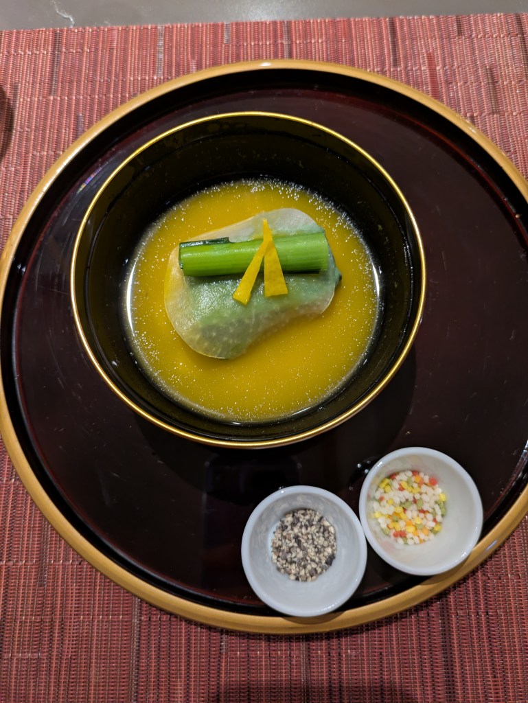 A bowl of vivid yellow soup with some artfully arranged vegetables
