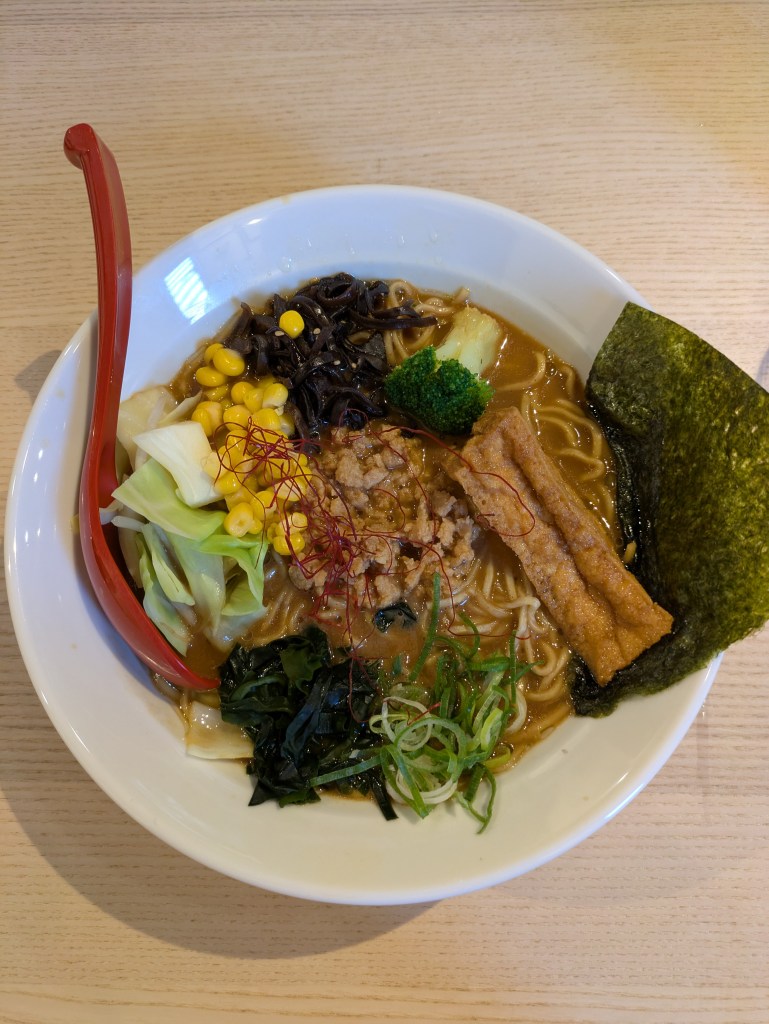 A bowl of ramen with a brown broth topped with seaweed, tofu, and lots of different vegetables