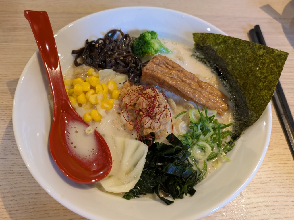 A bowl of ramen with a creamy broth topped with seaweed, tofu, and lots of different vegetables