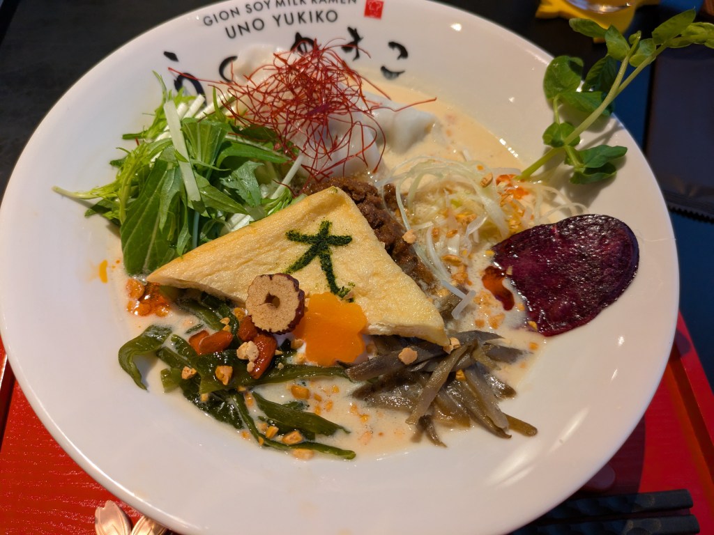 A big bowl of ramen with a creamy broth, lots of vegetables, some tofu, soy meat and a couple of gyoza
