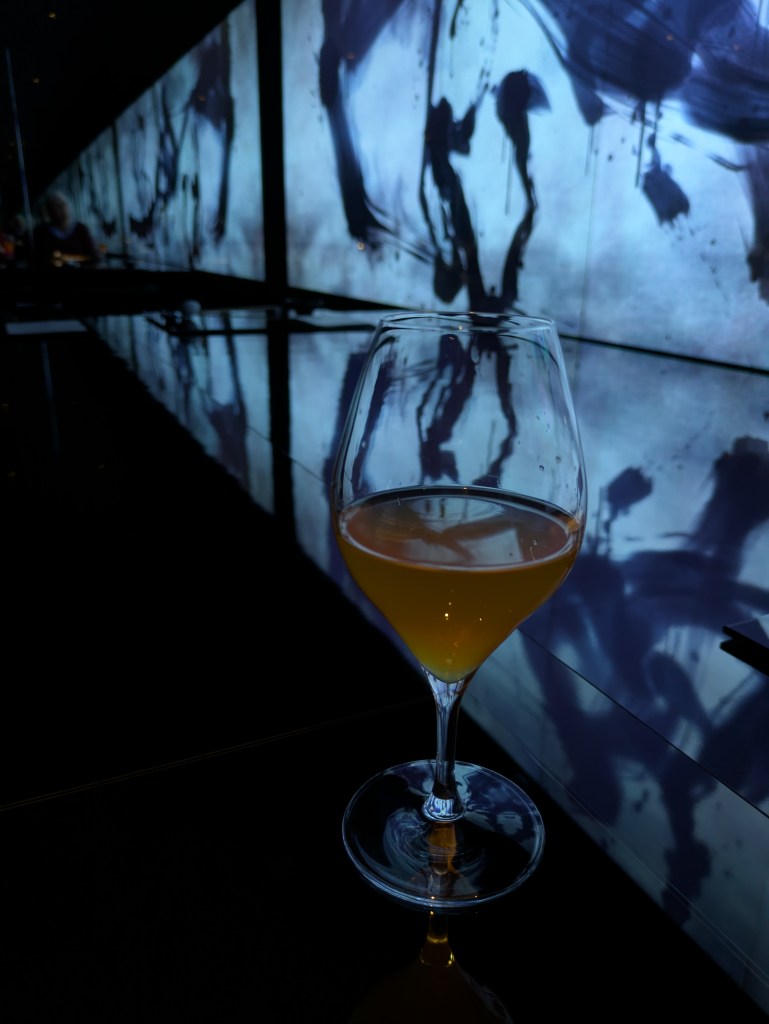 A glass of kombucha in front of the digital art work