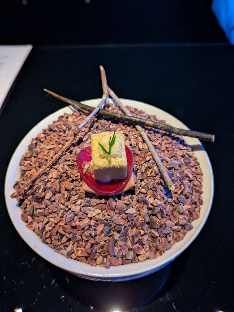 A small crackers with a pickled vegetable and a rectangle of vegan cheese on top