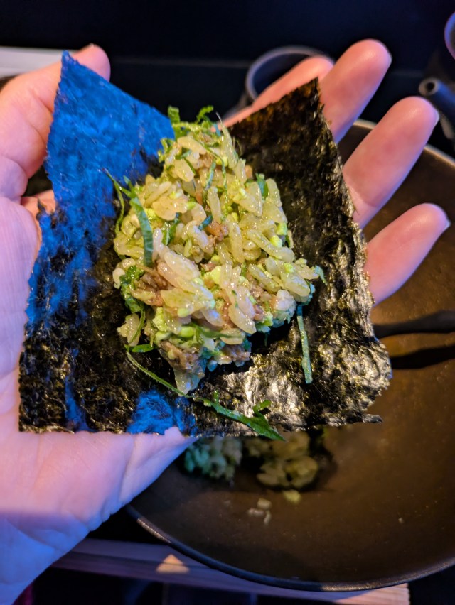 A hand holding the nori sheet flat with the rice heaped on top, ready to roll into handmade sushi